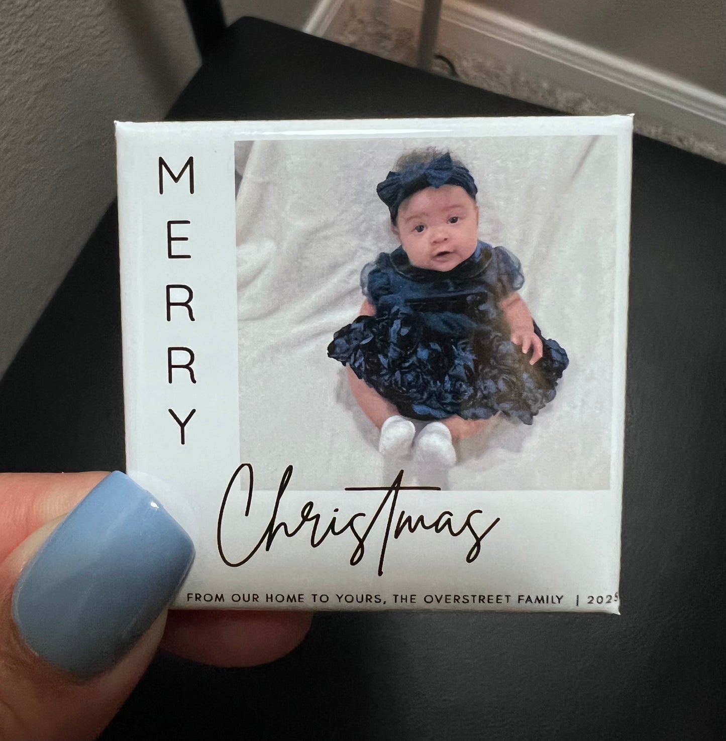 Christmas photo magnet with a baby in a blue dress and matching headband, held by a hand.