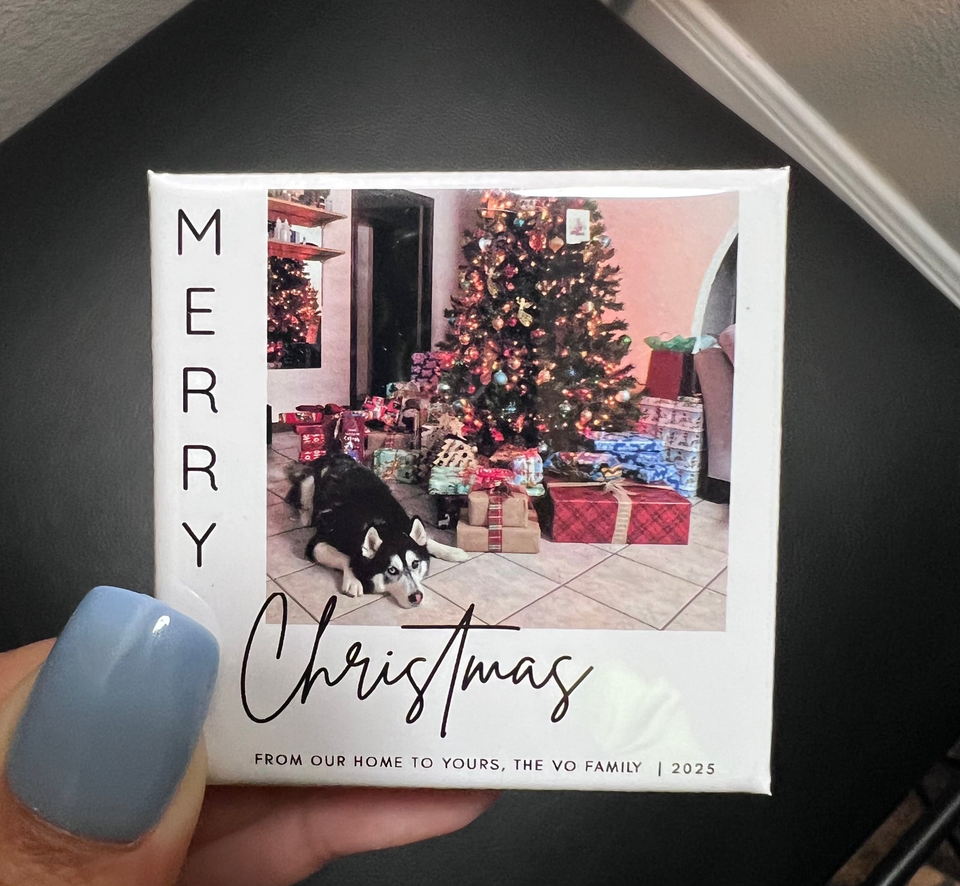Christmas photo magnet with a dog and Christmas tree, held by a person with light blue nail polish.
