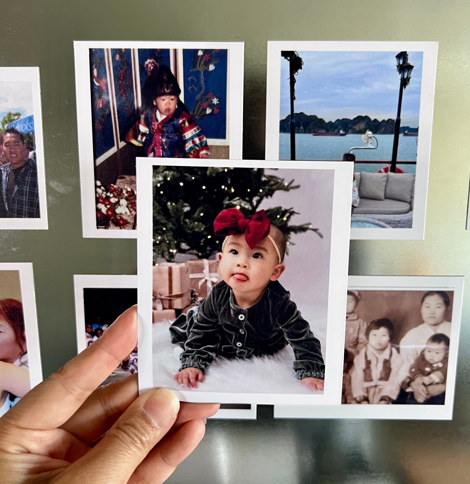 Collection of family photos displayed on a wall with a hand holding a photo of a child.