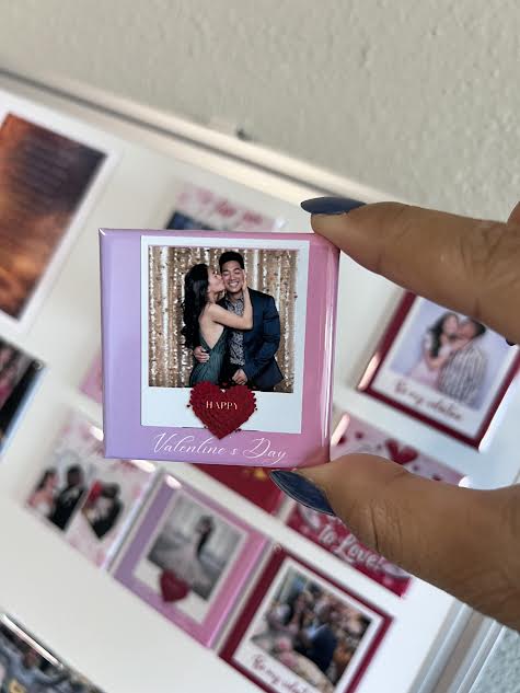 Hand holding a small photo magnet with a Valentine's Day design, surrounded by other decorative frames.