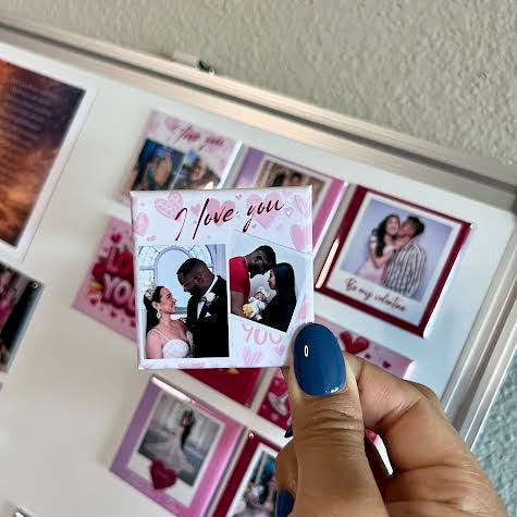 Hand holding a photo magnet with 'I love you' and photos of a couple, in front of a photo collage.
