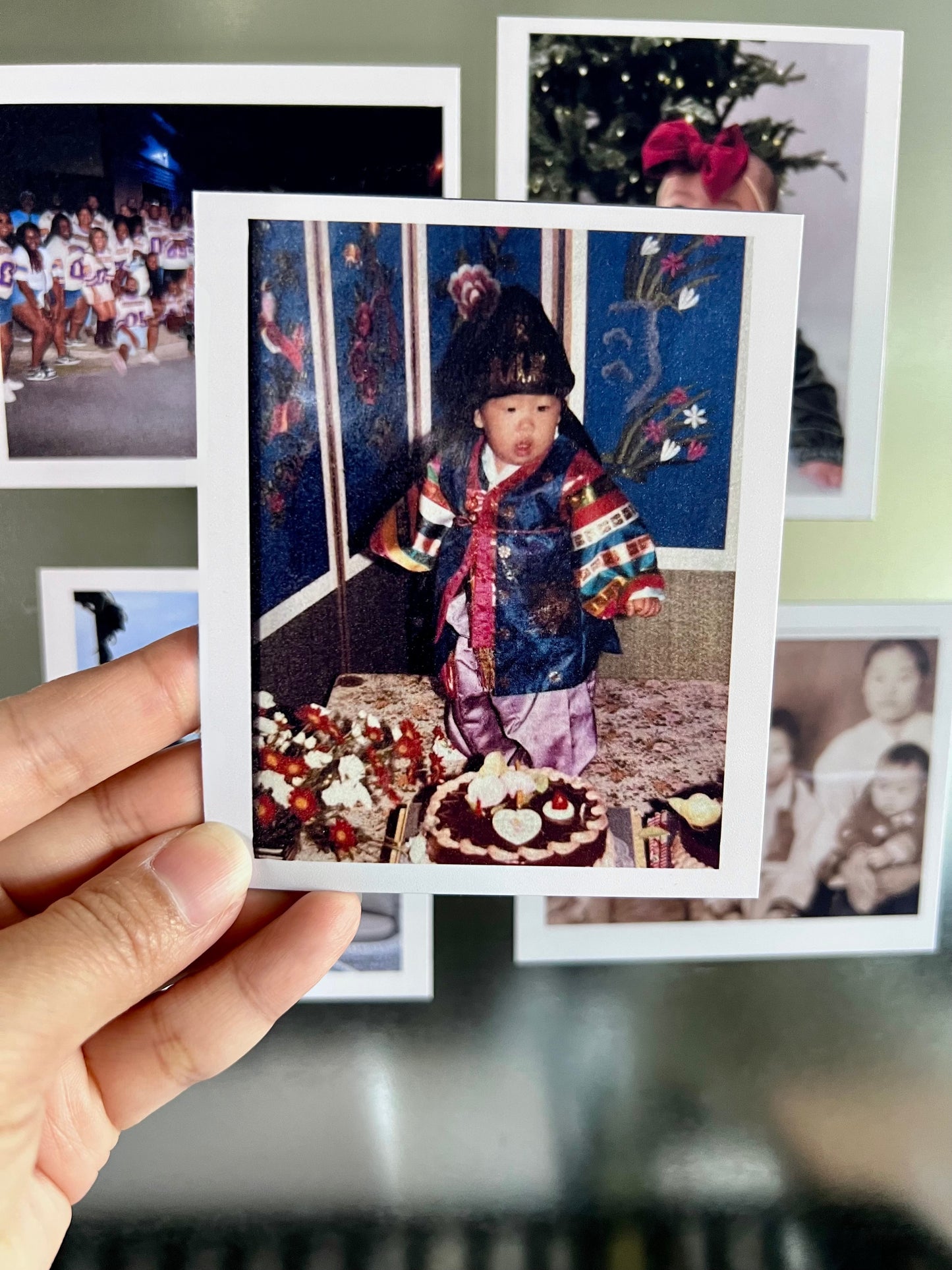 Person holding a flexible photo magnet of a child in a colorful outfit with a cake and decorations.