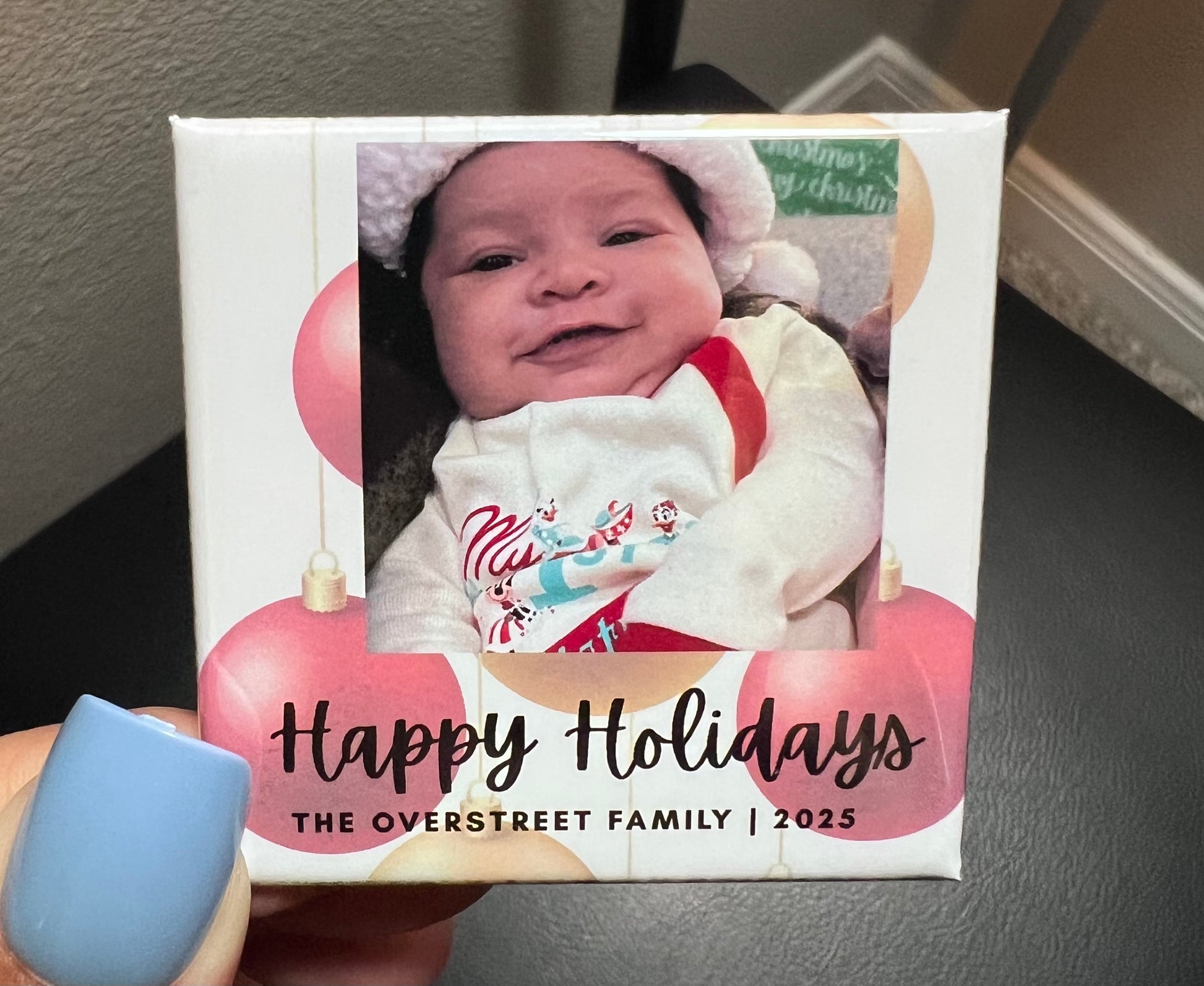 Photo magnet with a baby photo and 'Happy Holidays' text, held by a person.
