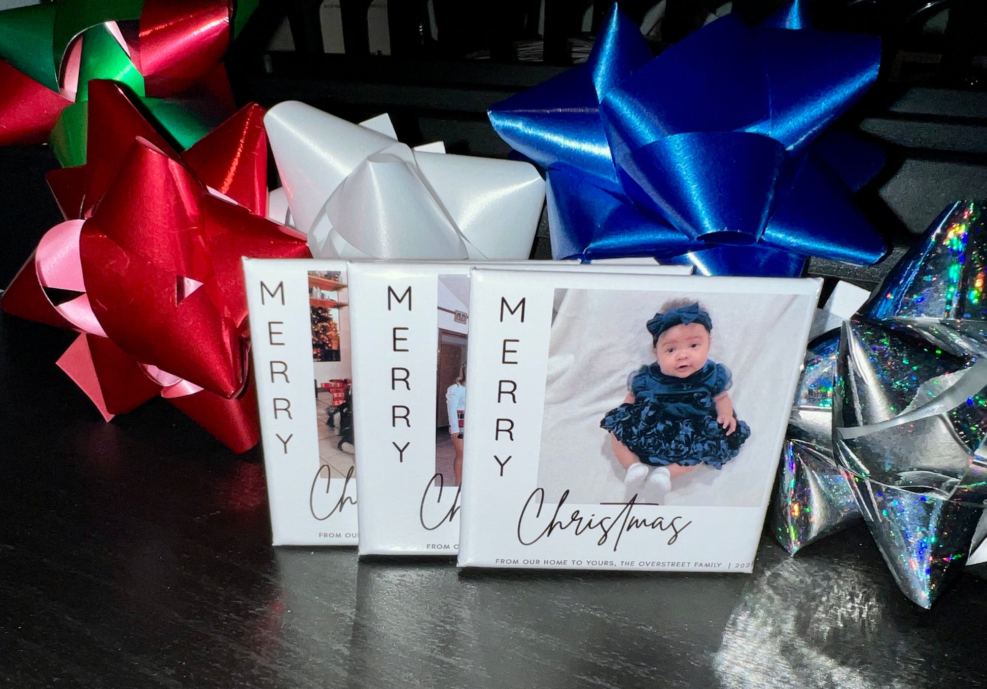 Three Christmas photo magnets with red, blue, and silver bows on a dark surface.